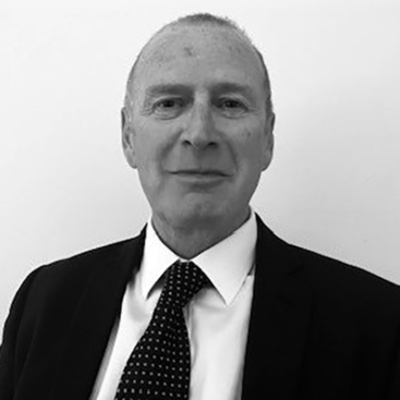 A man in a suit and tie is smiling at the camera against a plain white background. He has short hair and appears confident and approachable.