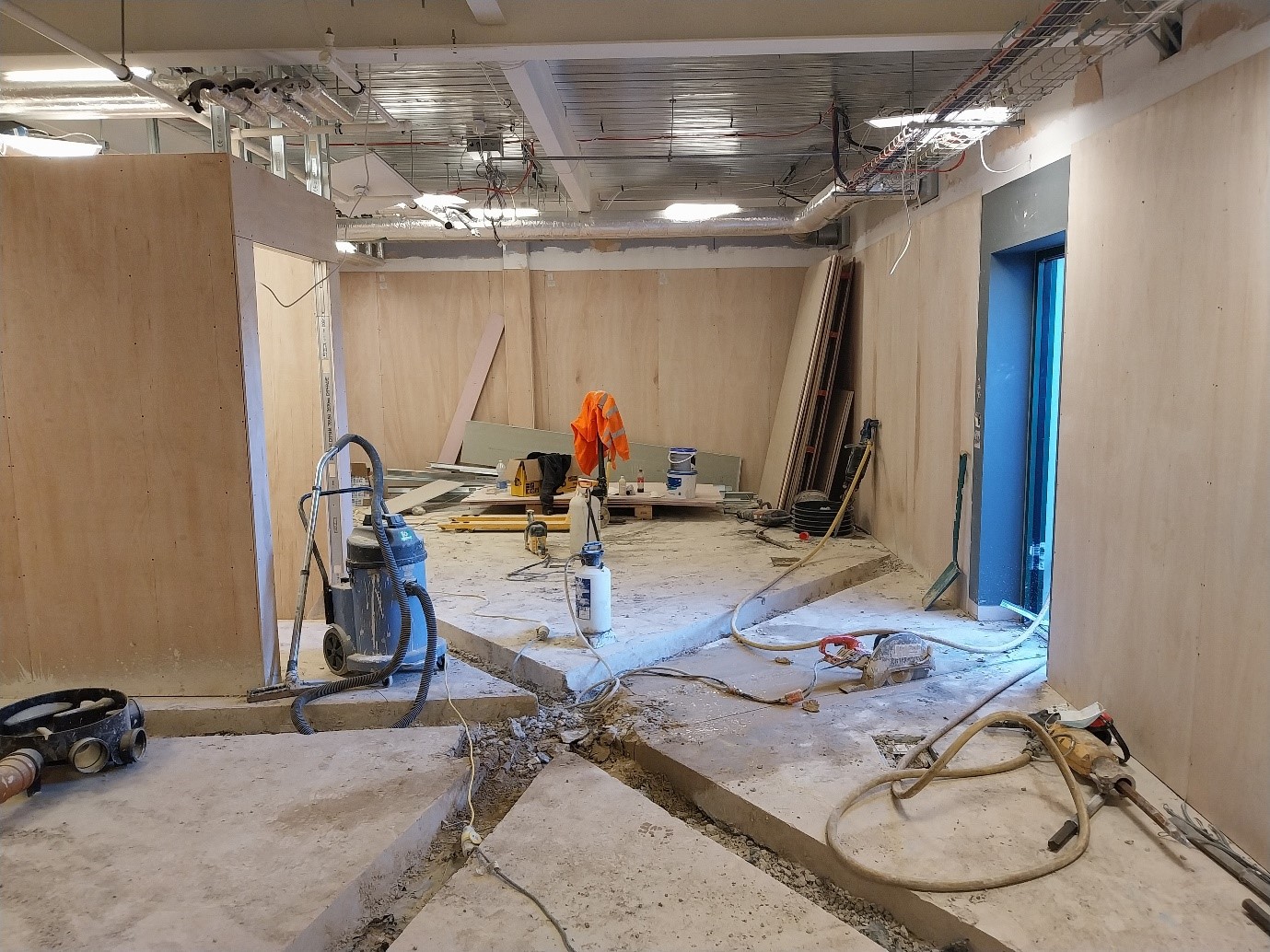 A construction site is depicted with unfinished walls and a cluttered floor. Tools and materials are scattered throughout, indicating ongoing renovation work.