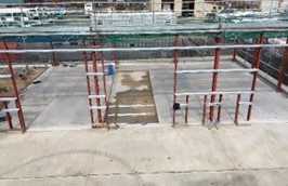 A construction site is visible, featuring a partially completed structure with exposed steel framework and a concrete floor. Scaffolding and construction materials are present, indicating ongoing work.